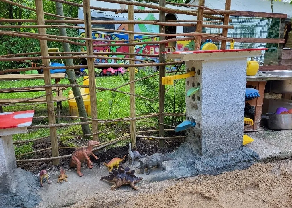 Spielzeug-Dinosaurier im großen Sandkasten der Matschküche