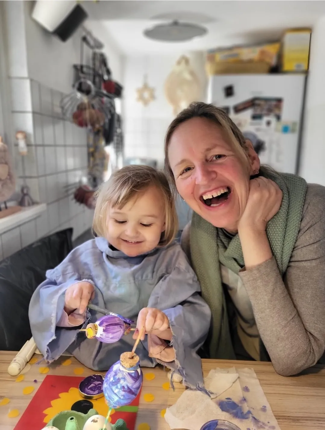Mutter und Kind bemalen gemeinsam lachend Ostereier