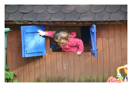 Kind öffnet im Garten des Spielegarten Lindental die Läden der Gartenlaube